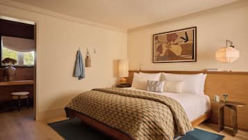 A bedroom with a bed, bedside table, lamp, artwork, and a view of the outdoors.