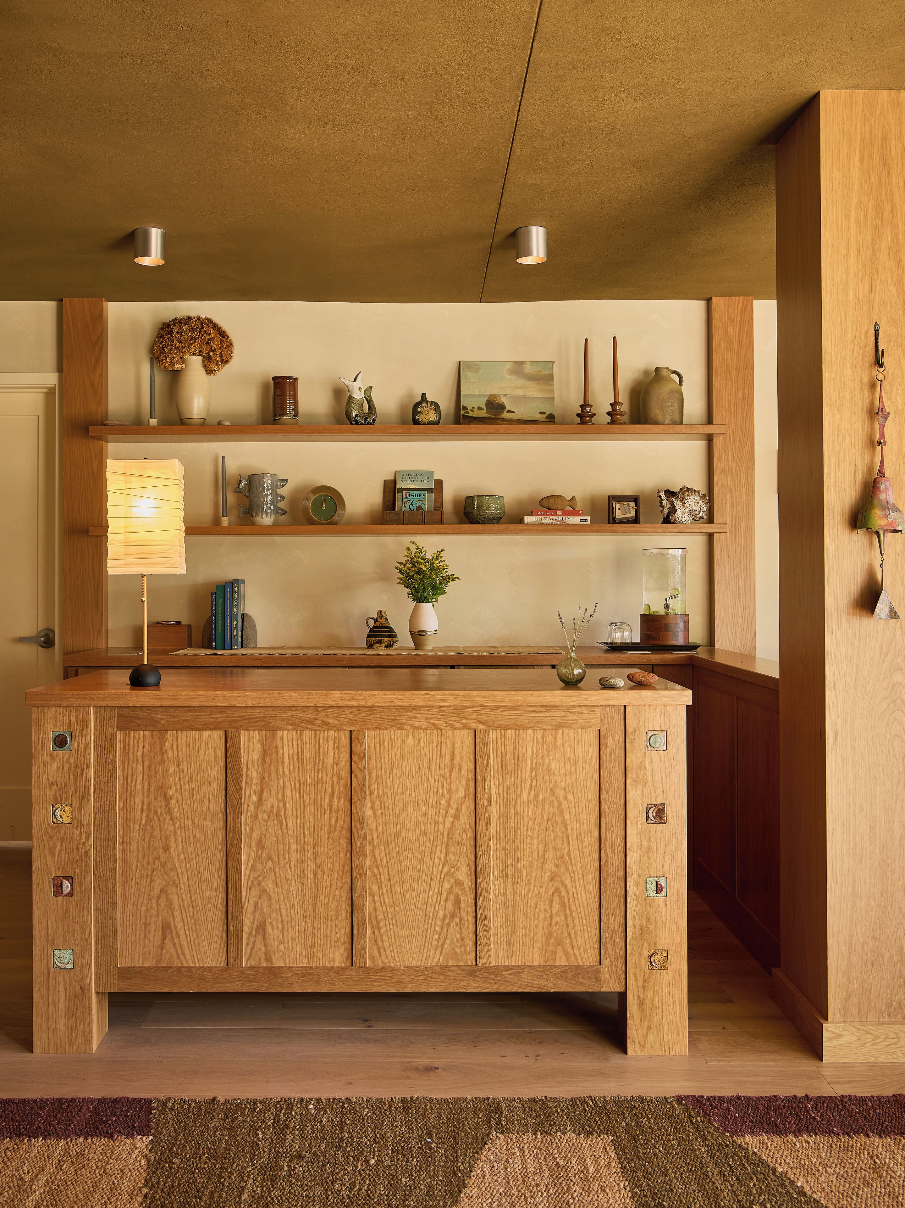 Een houten keukeneiland met inbouwplanken, een hanglamp en diverse decoratieve objecten.