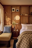 A cozy bedroom with a wooden headboard, a bedside table with a lamp, a vase with flowers, and a bed with a floral bedspread.