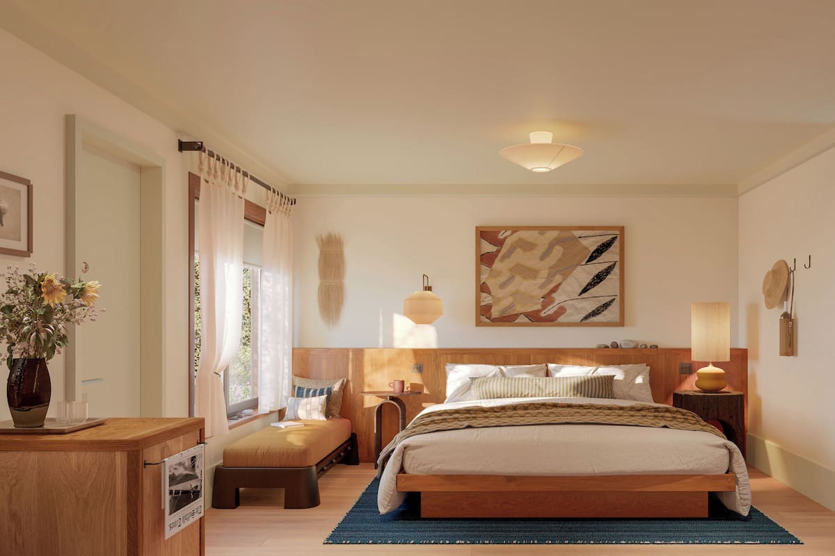 A bedroom with a bed, bedside tables, a nightstand, a lamp, a painting, a robe, and a bathroom door.