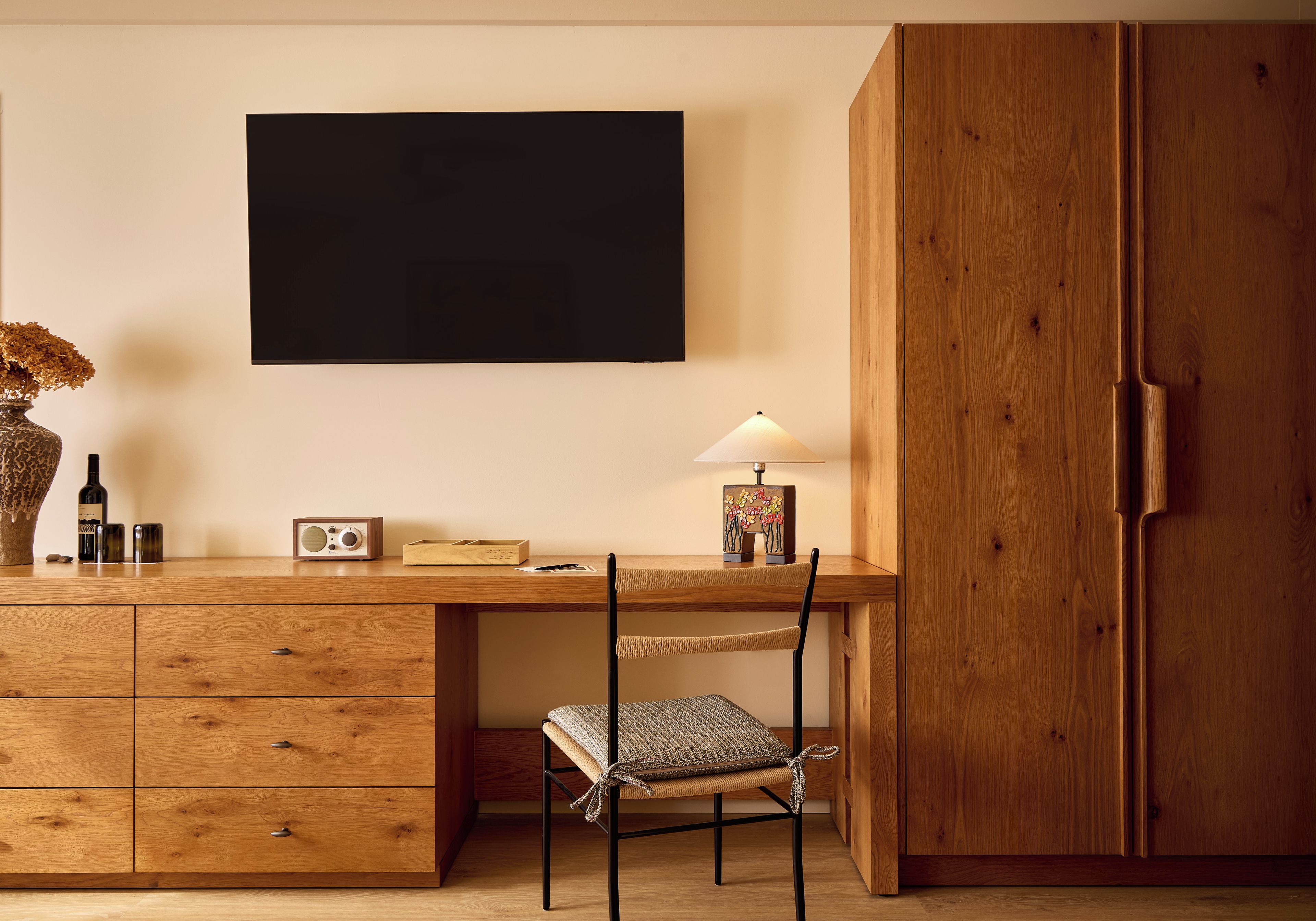 Ein Schreibtisch aus Holz mit Schubladen, ein Stuhl, eine Lampe und ein gerahmtes Bild an der Wand.