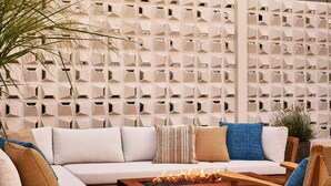 A modern outdoor seating area with a sofa, cushions, a wooden coffee table with a fire feature, and a decorative wall with geometric patterns. - Oyster Estate (Greenport)