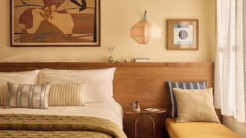 A hotel room with a large bed, a smaller sofa, a bedside table with a lamp, and a framed artwork on the wall.