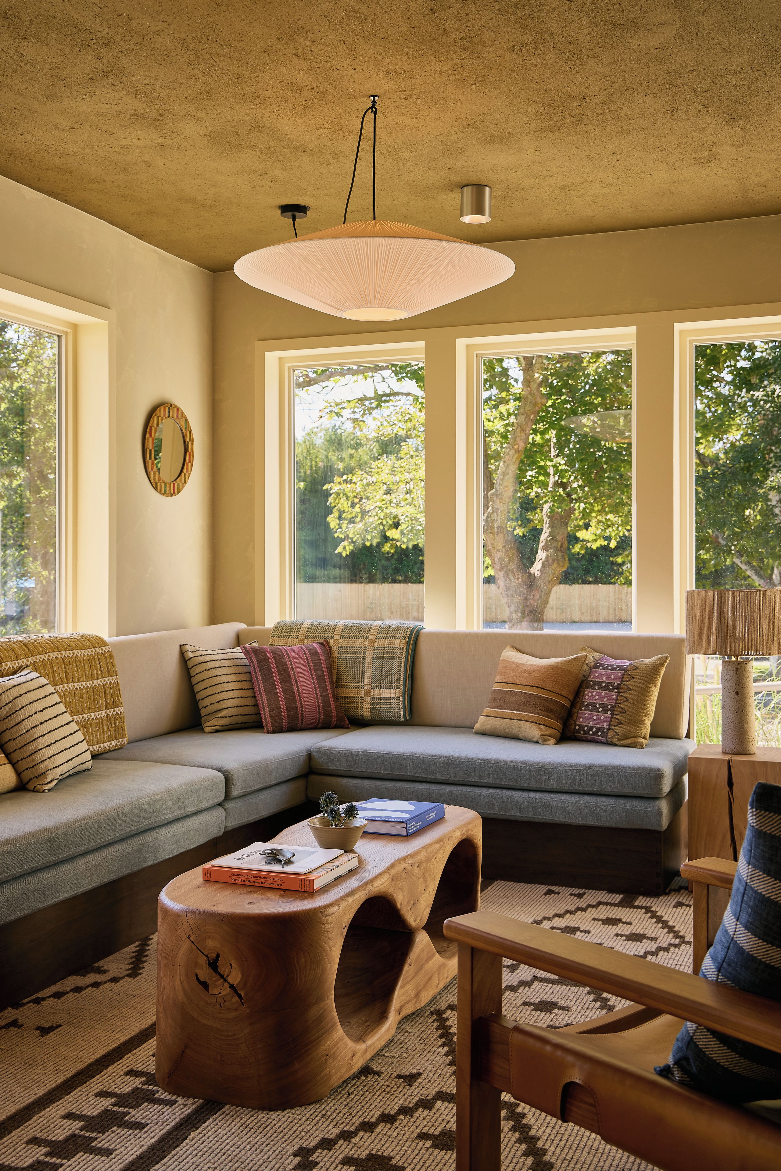 A modern living room with a sectional sofa, a wooden coffee table, and a large window providing a view of trees.
