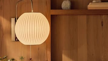 Un mur en bois avec une lampe fixée au mur, une étagère ornée d’objets décoratifs et une table de chevet avec un coussin.