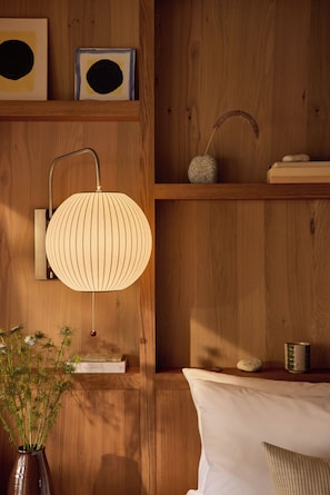 Una pared de madera con una lámpara de pared, una repisa con adornos y una mesita de noche con un almohadón.