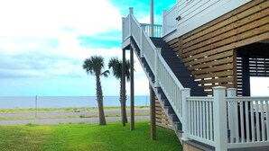 Ein Haus mit einer Holzterrasse und einer Treppe, die zu einem Balkon mit Blick aufs Meer führt.