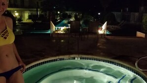 Ein Schwimmbeckenbereich bei Nacht mit Whirlpool, Liegestühlen und einem Gebäude im Hintergrund.