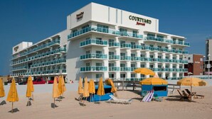 A Courtyard hotel with multiple balconies, beach umbrellas, and beach chairs. - Miramar Condominiums (Ocean City)