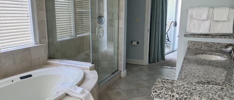 Un bany amb una banyera gran, un espai de dutxa amb envàs de vidre i un lavabo amb taulell de granat.