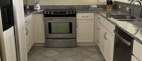 A compact kitchen with white cabinets, a built-in microwave, a stove, and a dishwasher.