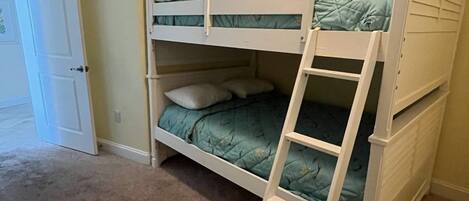 Una cama litera con escalera, una puerta y suelo cubierto de alfombra.