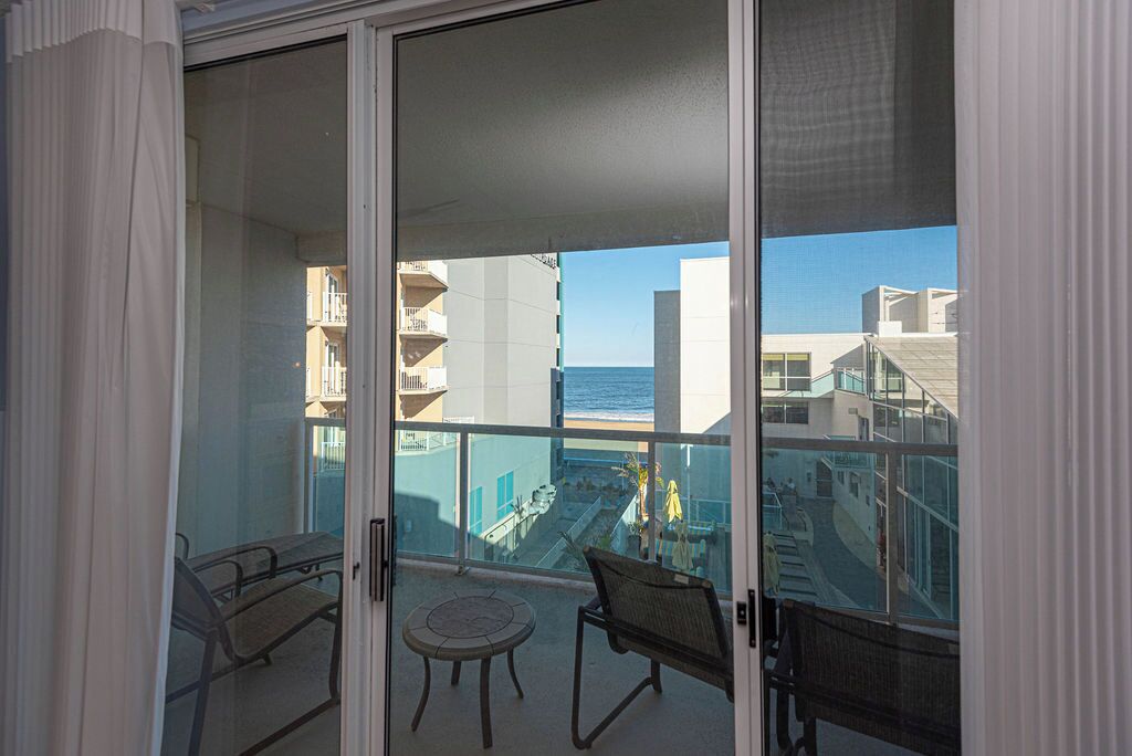 A balcony with a table and chairs, overlooking a coastal area with buildings and a clear sky.