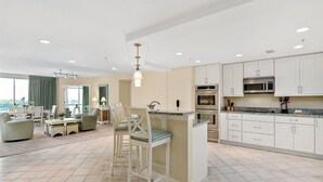 A spacious kitchen with white cabinets, a central island, and a dining area with chairs and a table. - Miramar Condominiums (Ocean City)