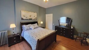 Un dormitorio con cama, mesitas de noche, cómoda, silla, ventilador de techo y un espejo grande.