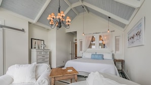 Un dormitorio con una cama grande, una mesa de madera, muebles blancos, una araña y un cuadro en la pared.