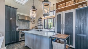 Una cocina con una isla grande, armarios oscuros y faroles colgantes.