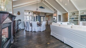 Amplia sala de estar con techo alto, chimenea, mesa de comedor con sillas y un sofá blanco grande.