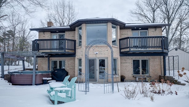 Une maison à deux étages avec un balcon, une terrasse couverte avec des chaises et un jacuzzi.