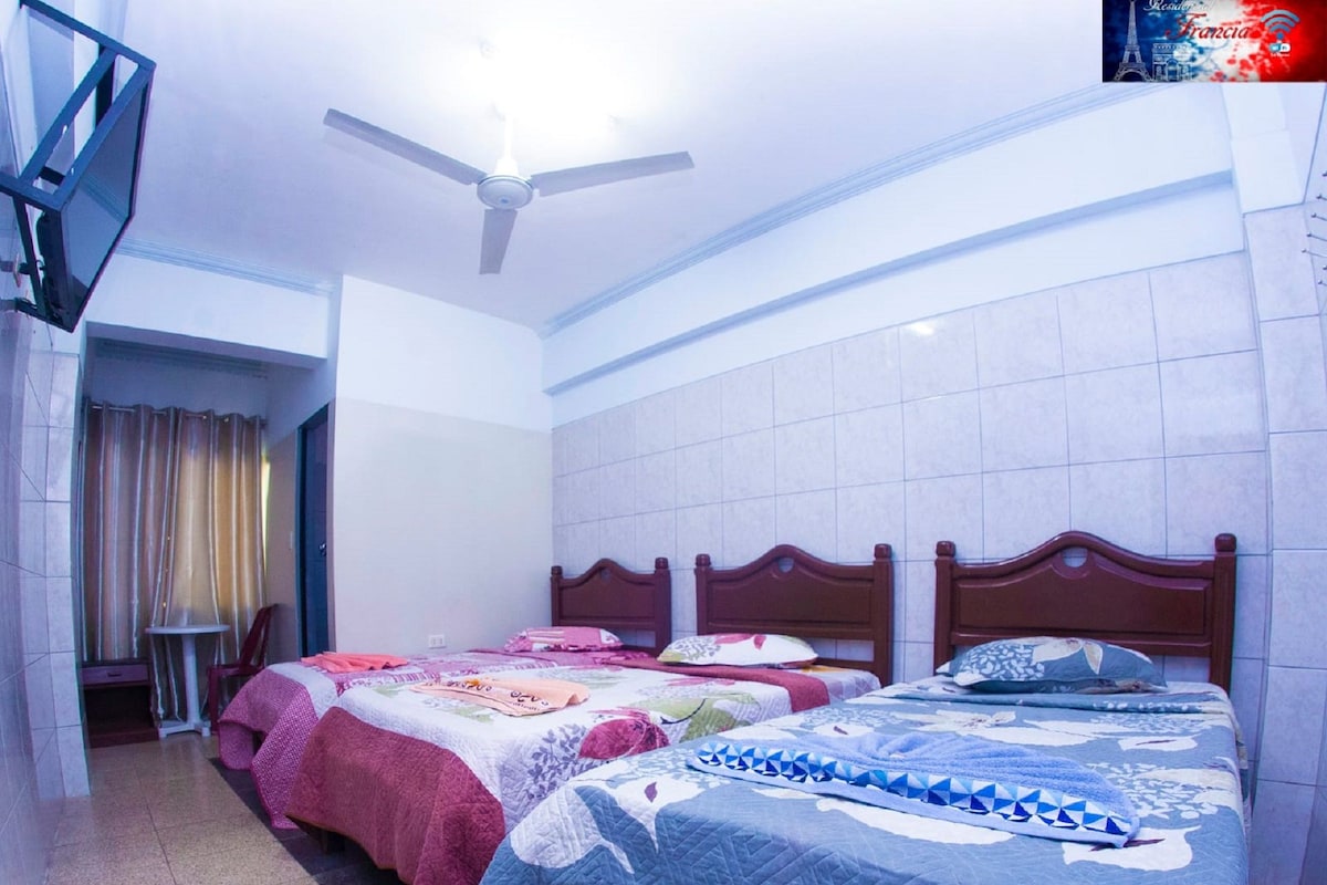Habitación de hotel con dos camas, ventilador de techo y una pequeña mesa con sillas.
