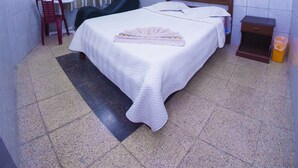 A bedroom with a bed, a chair, a nightstand, a trash bin, and a ceiling fan. - residencial francia - Hostel (Santa Cruz)