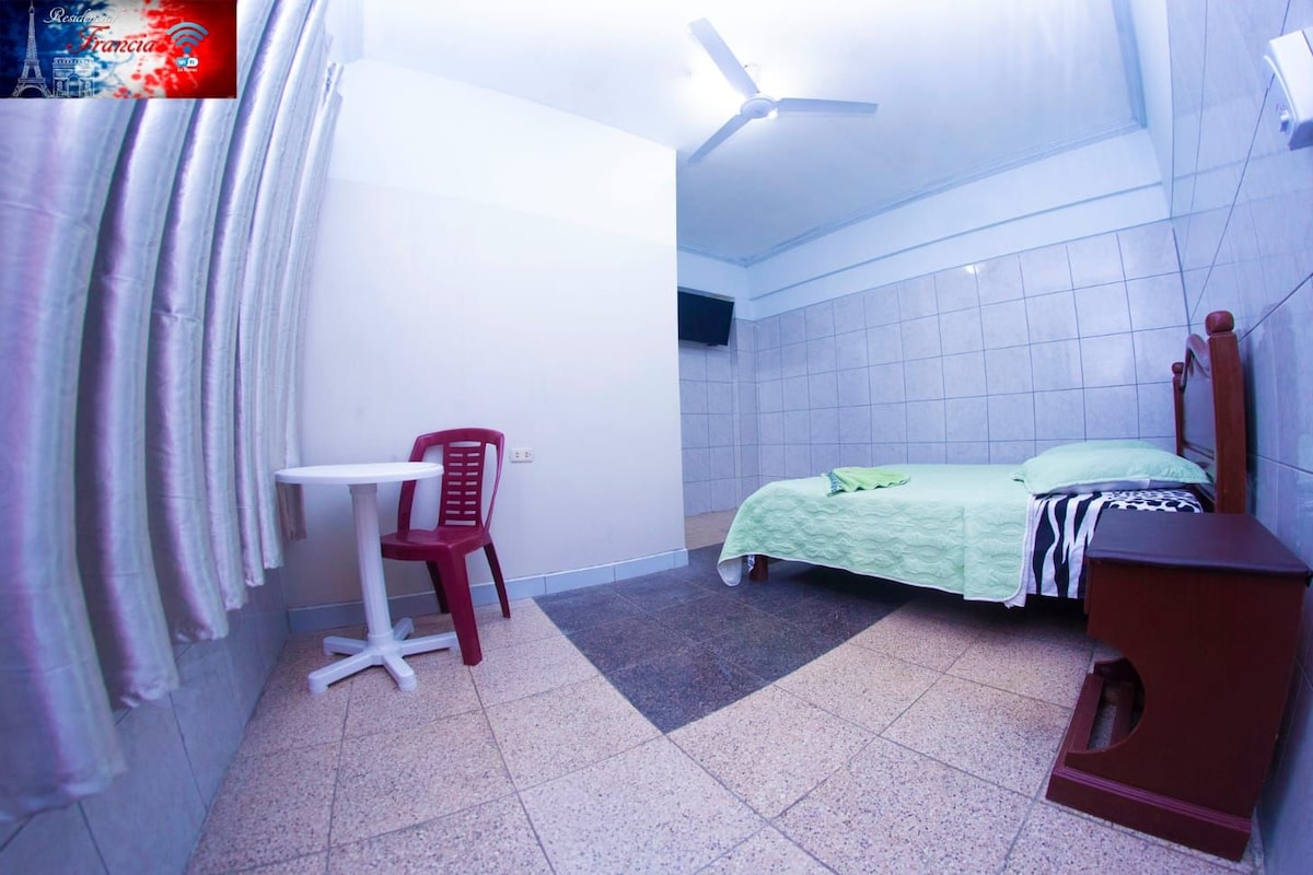 A small, clean room with a bed, a desk, and a chair.