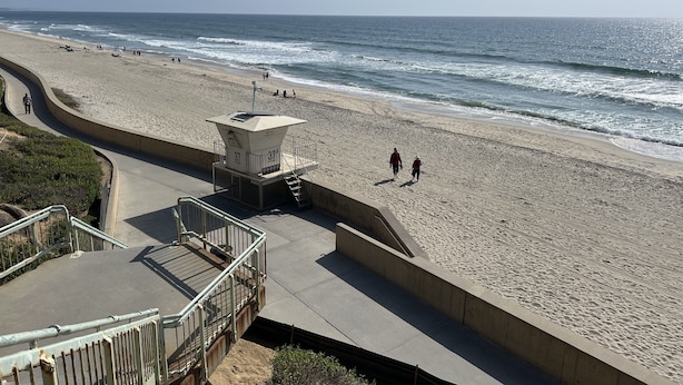 A beach with a lifeguard tower, a curved walkway, and a sandy shore.