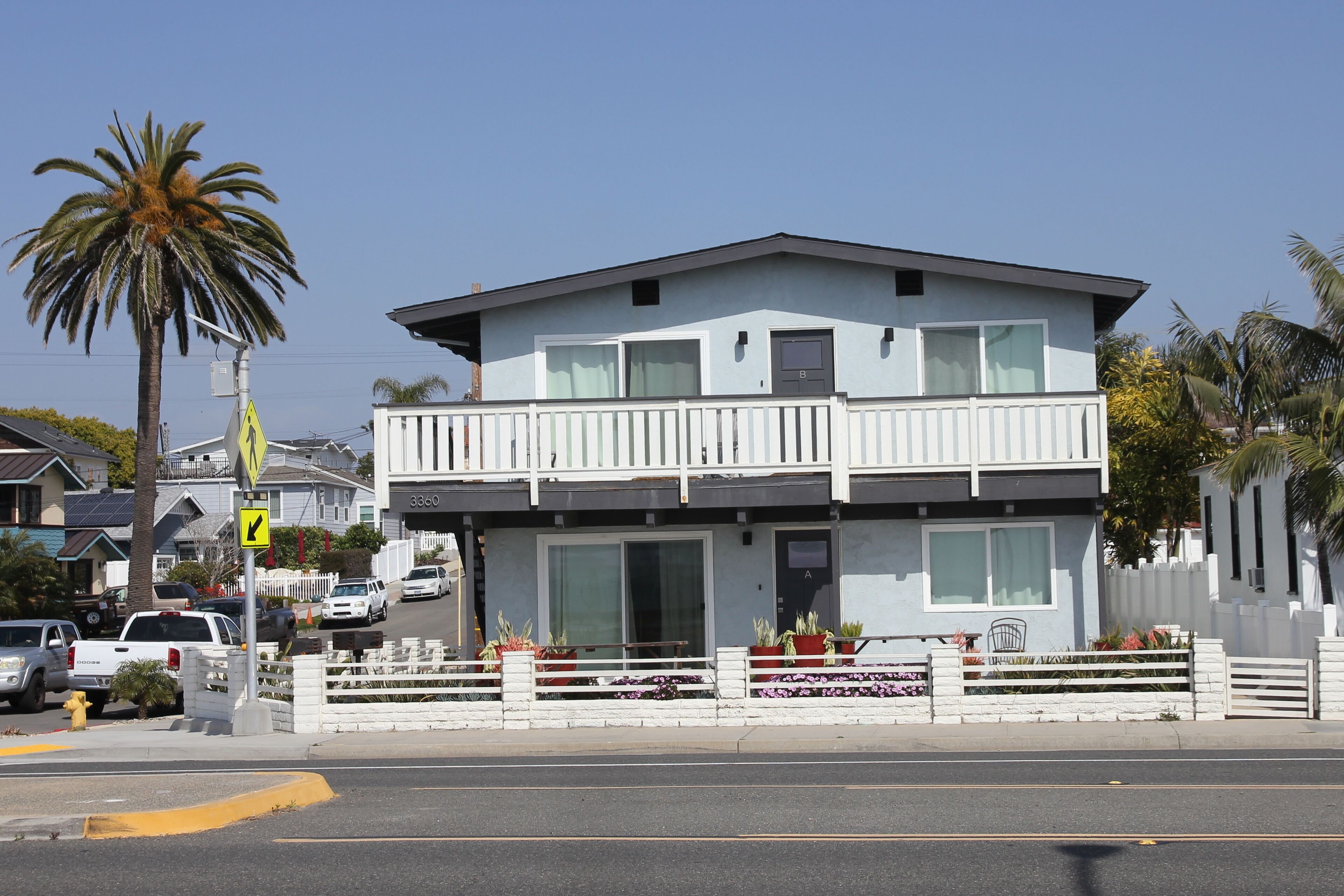 A two-story building with a balcony, a white picket fence, and a street view.