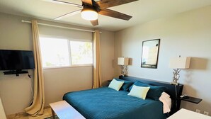 A bedroom with a bed, a ceiling fan, a TV, a window with curtains, a bedside table, and a nightstand.