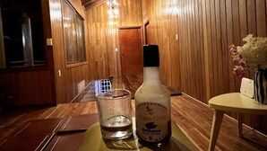 Un intérieur en bois avec une table, une bouteille de Colosina et un verre.
