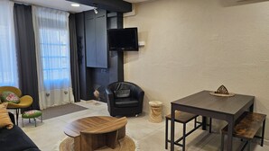 Un saló modern amb un sofà de pell negra, una taula de centre de fusta, una butaca de pell negra i una taula rodona petita amb un tamboret trenat.