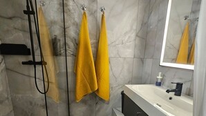 Un bany modern amb plat de dutxa envoltat de vidre, un rentapeus blanc i un mirall gran.