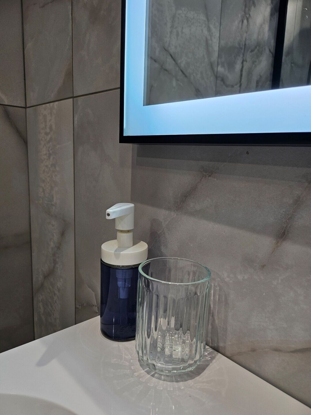 A bathroom with a marble wall, a mounted TV, a soap dispenser, and a glass container.