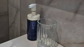 A bathroom with a marble wall, a mounted TV, a soap dispenser, and a glass container.