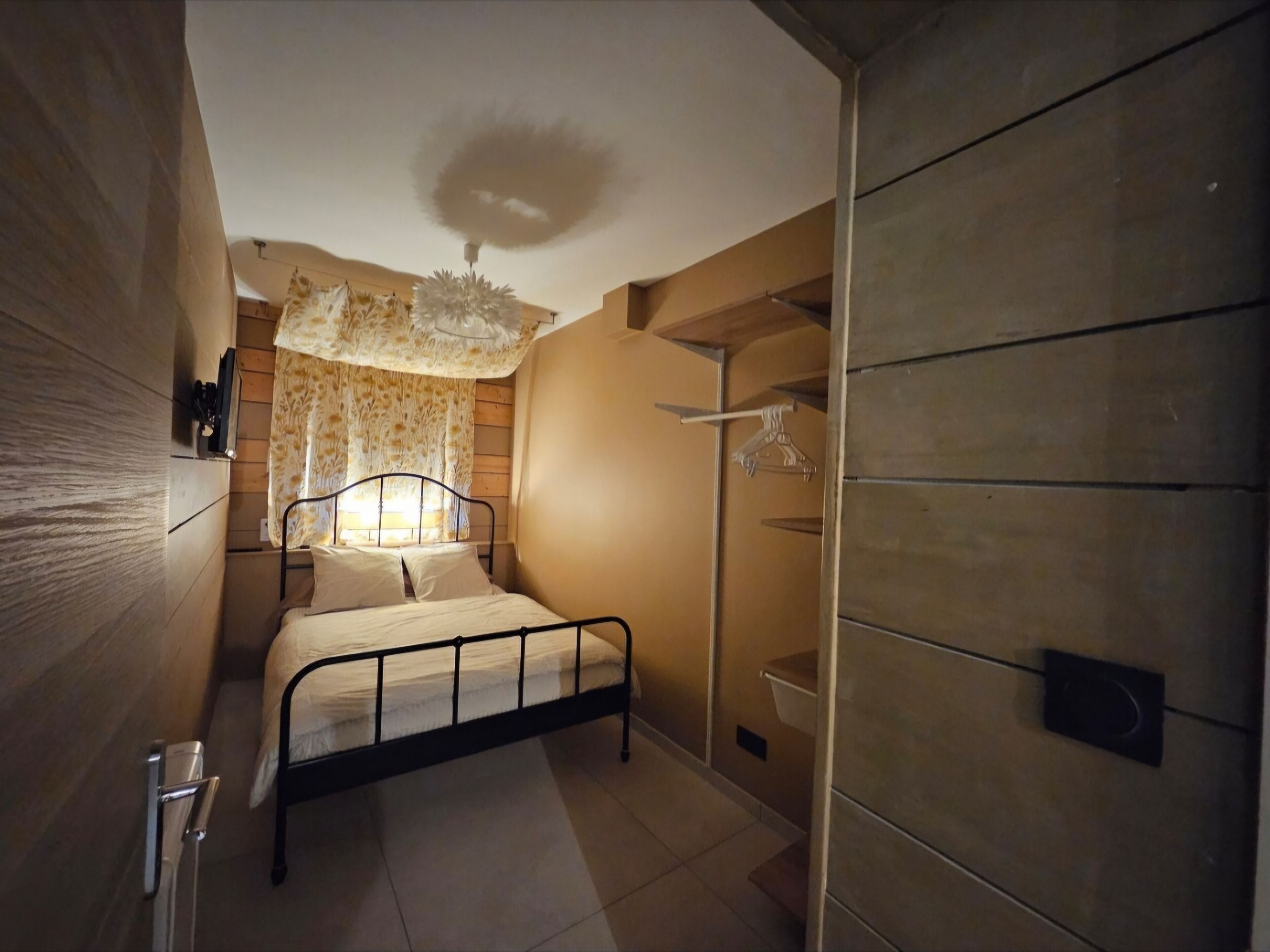 A bedroom with a bed, a hanging light fixture, a wardrobe, and a window with curtains.