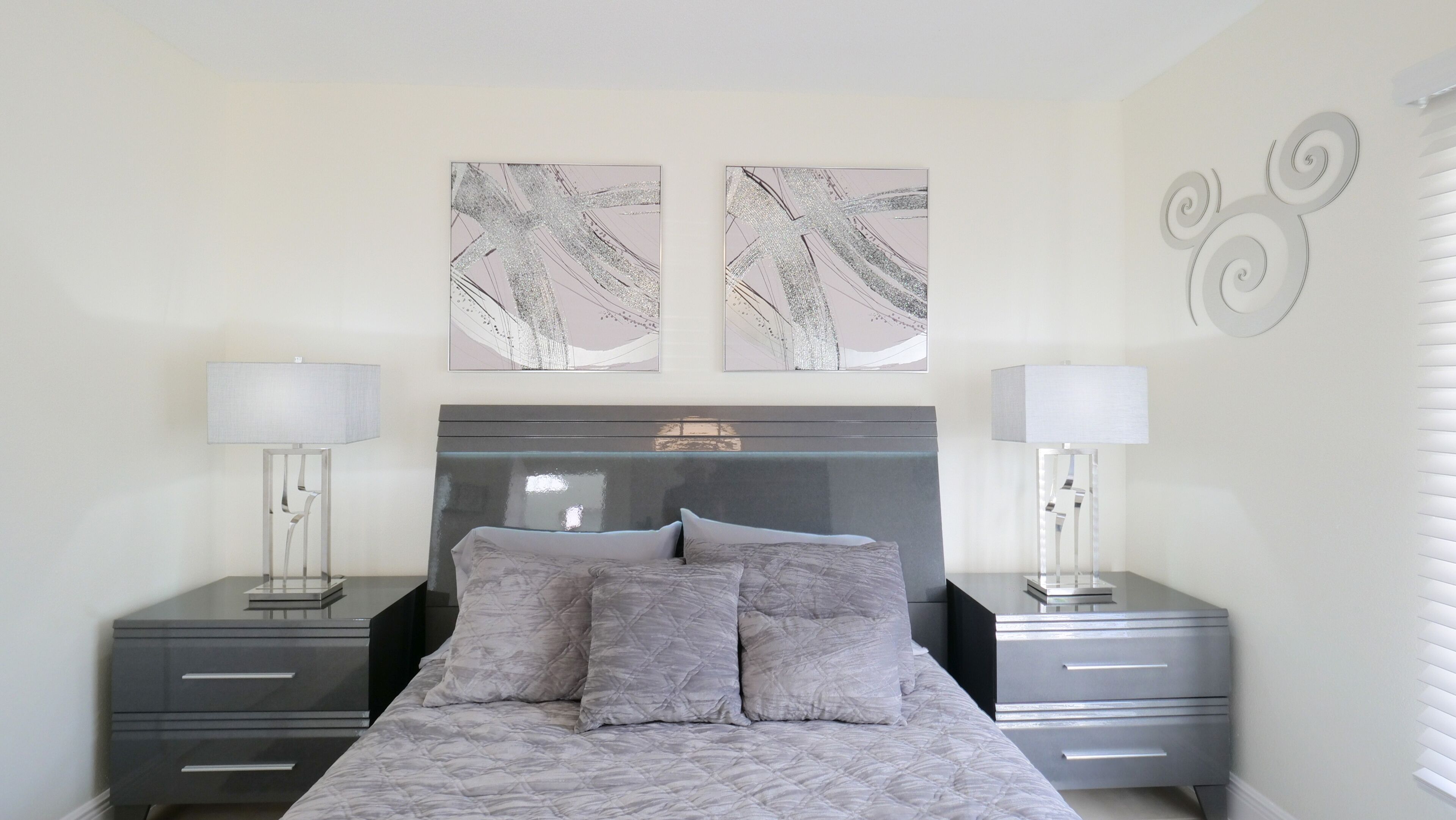 Une chambre à coucher comprenant un lit, deux tables de chevet, deux lampes fixées au mur et des œuvres d’art abstraites.
