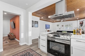 Una cocina moderna con armarios blancos, estufa de acero inoxidable y techo de madera.