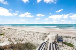 Ein Strand mit einer Holzpromenade, die zum Wasser führt, Sanddünen und einem klaren, blauen Himmel.