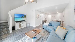 Ein modernes Wohnzimmer mit einem großen Flachbildfernseher, einem blauen Sofa, einem Holztisch und einer Treppe, die zu einer oberen Ebene führt.