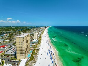 A coastal cityscape with a long sandy beach, a large hotel with multiple floors, and a clear blue sky.