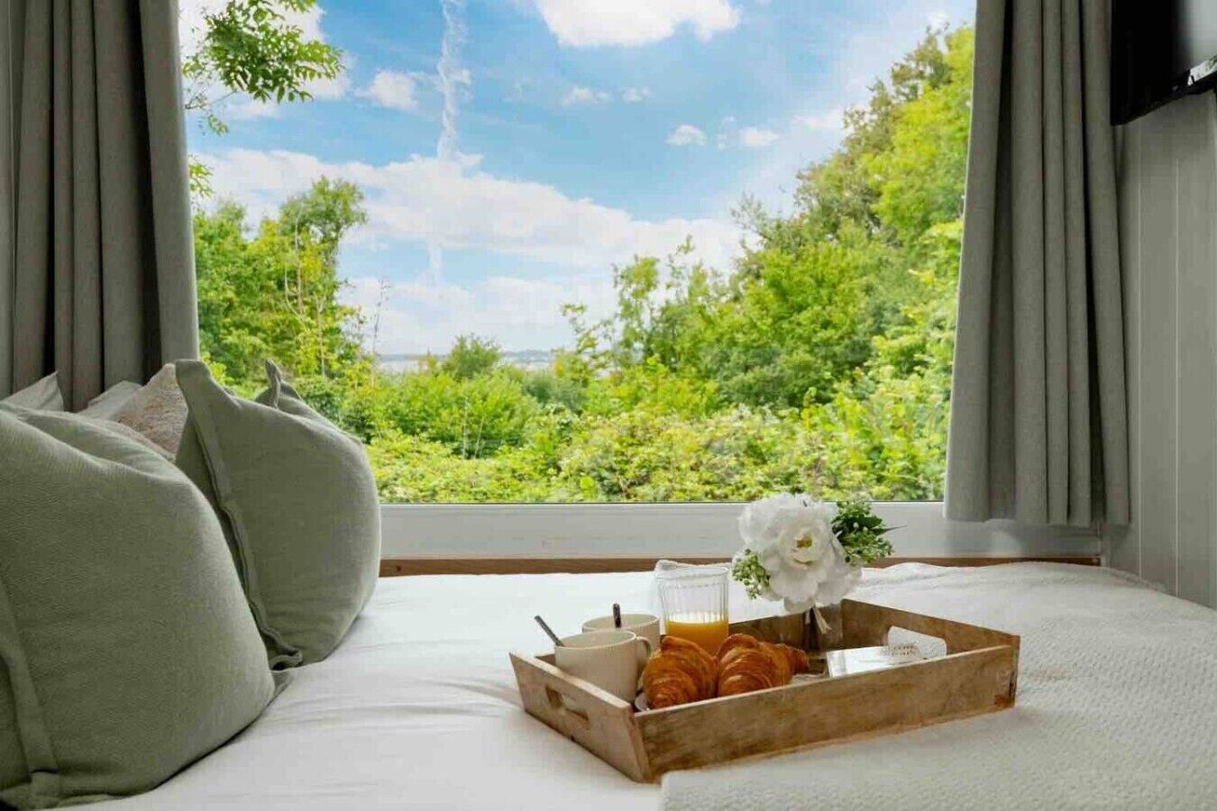 A bedroom with a bed, a tray with croissants, a glass of orange juice, and a flower.