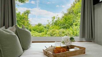 A bedroom with a bed, a tray with croissants, a glass of orange juice, and a flower.