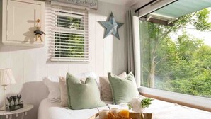 Une chambre avec un lit, des oreillers, un plateau avec des croissants et du jus, une décoration en forme d’étoile et une fenêtre donnant sur des arbres.