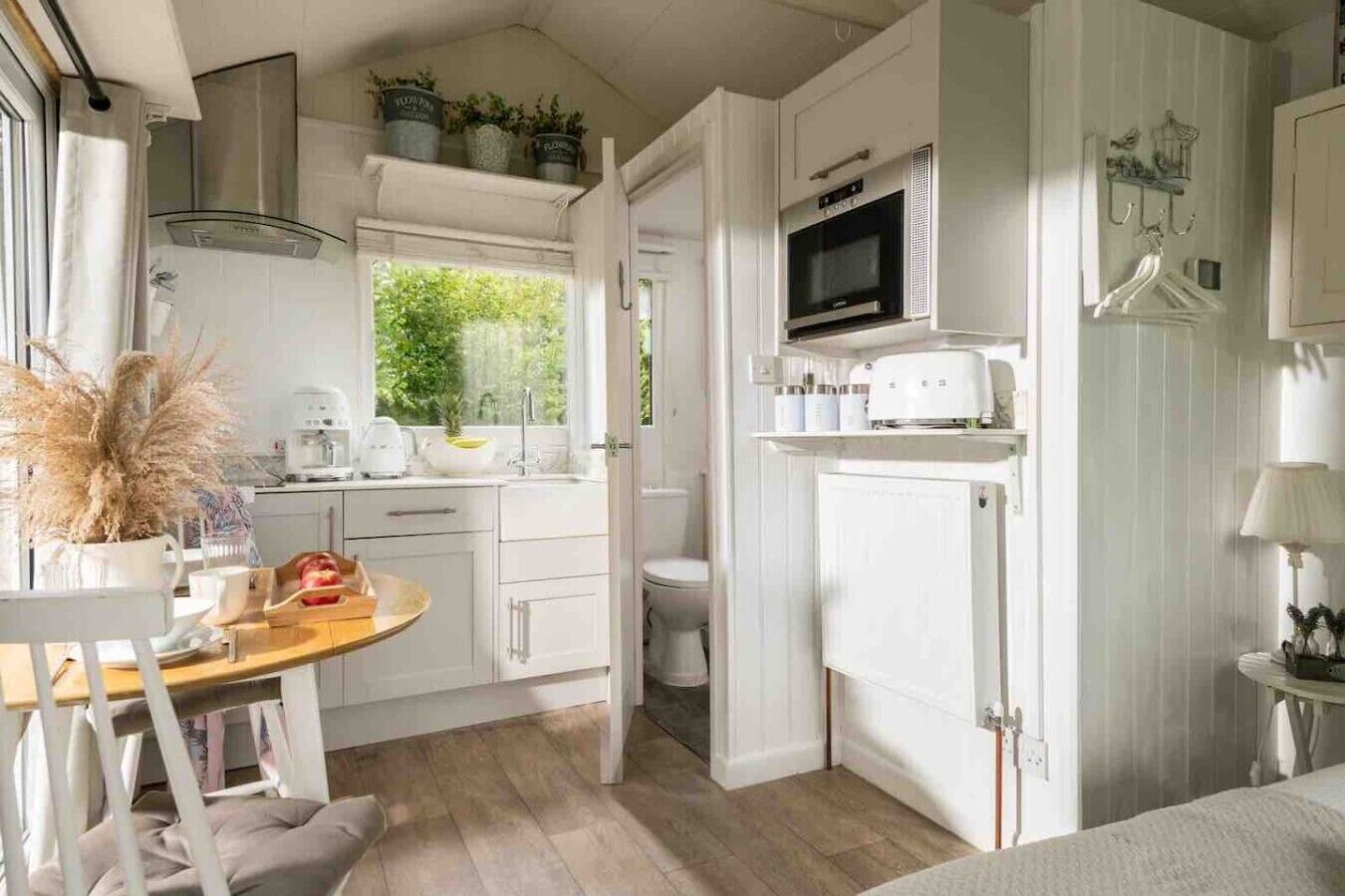 A compact kitchen with white cabinetry, a microwave, and a window overlooking greenery.
