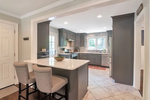 A modern kitchen with a central island, grey cabinets, and a white countertop.