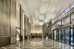 A modern hotel lobby with a reflective marble floor, a reception desk, and a decorative ceiling light fixture. - Wyndham Xiong'An (Baoding)