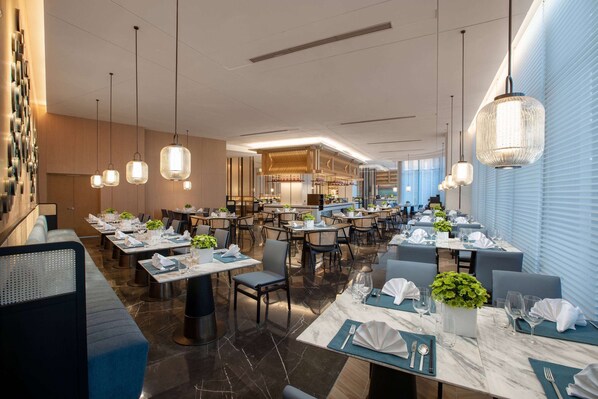 A modern dining area with multiple tables, chairs, and hanging pendant lights. - Wyndham Xiong'An (Baoding)