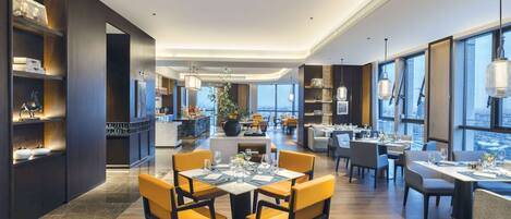 A modern hotel lobby with a central seating area, a bar, and a view of the city.