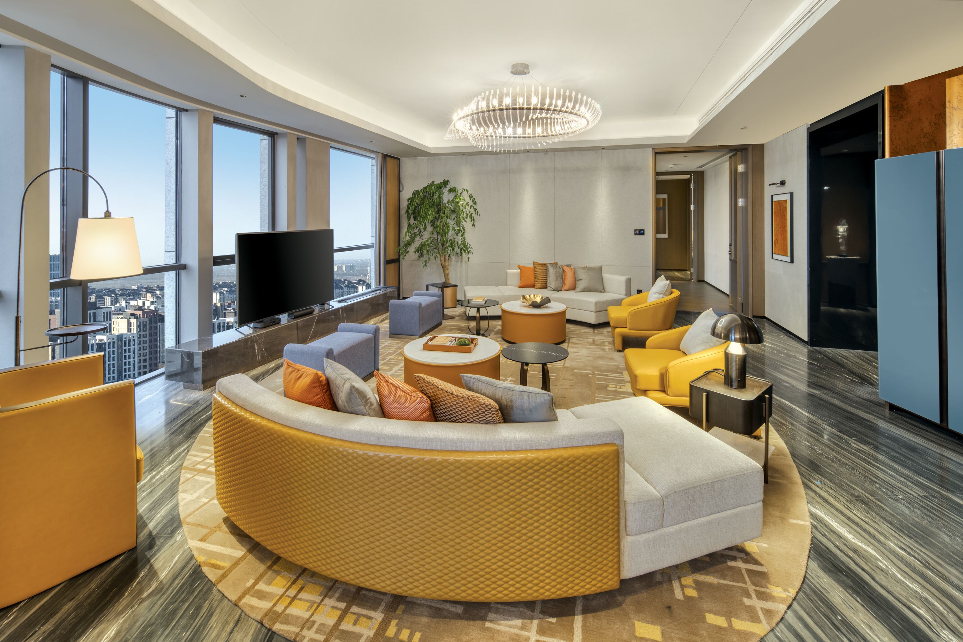 Een moderne hotel lobby met een gebogen bank, een televisie, een grote plant en uitzicht over de stad.