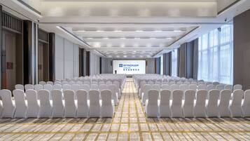 A conference room with rows of white chairs, a tiled floor, and a large screen displaying 'WYNDHAM'.